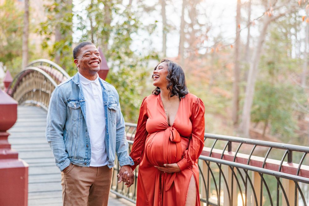 A couple shares a happy moment on a bridge during an autumn maternity photoshoot.