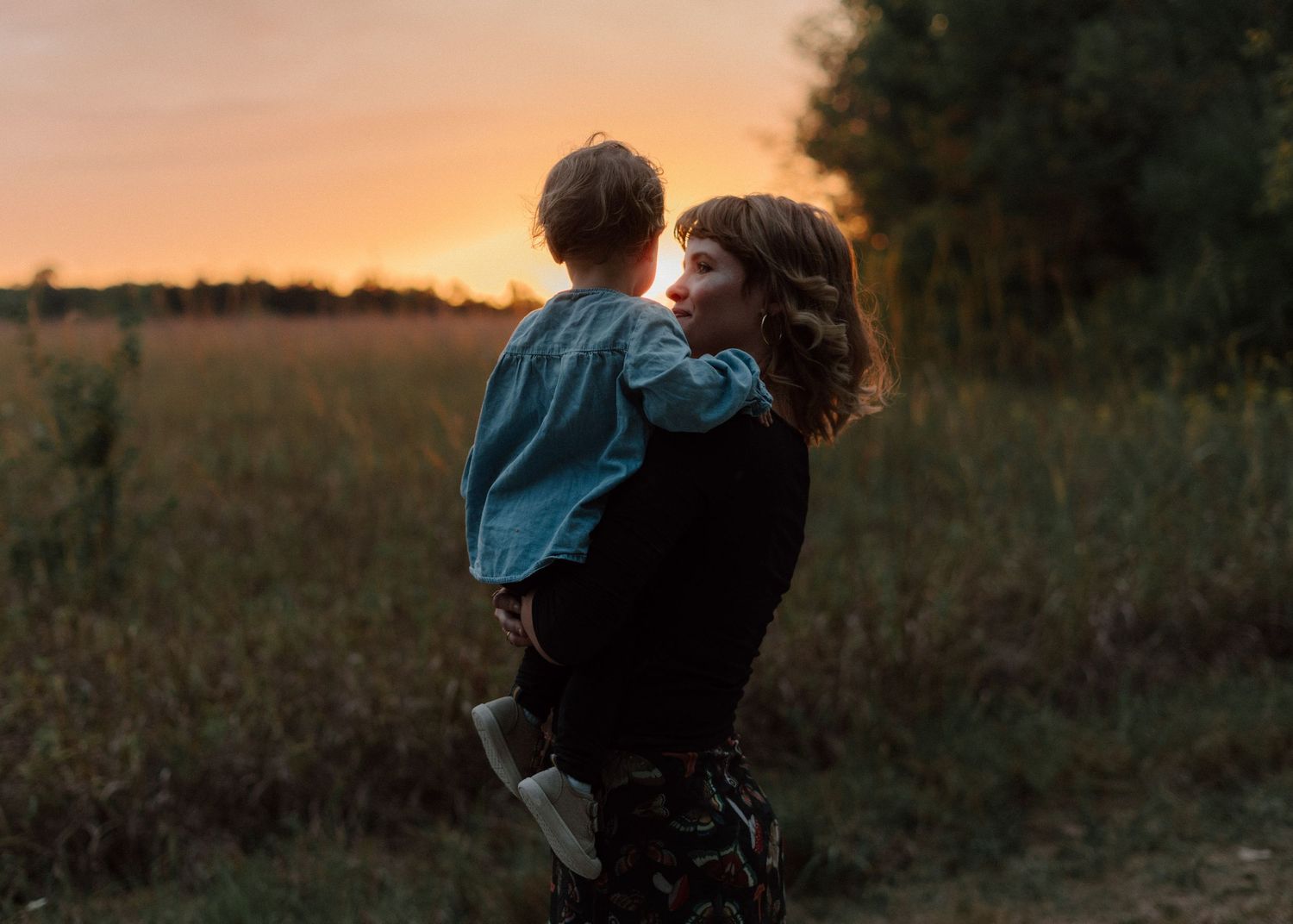 Silhouette of parent and child embracing in a golden field at sunset.