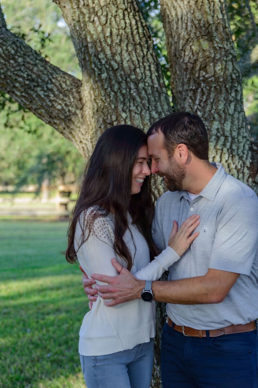 A romantic couple embraces while sharing an intimate moment against a tree.