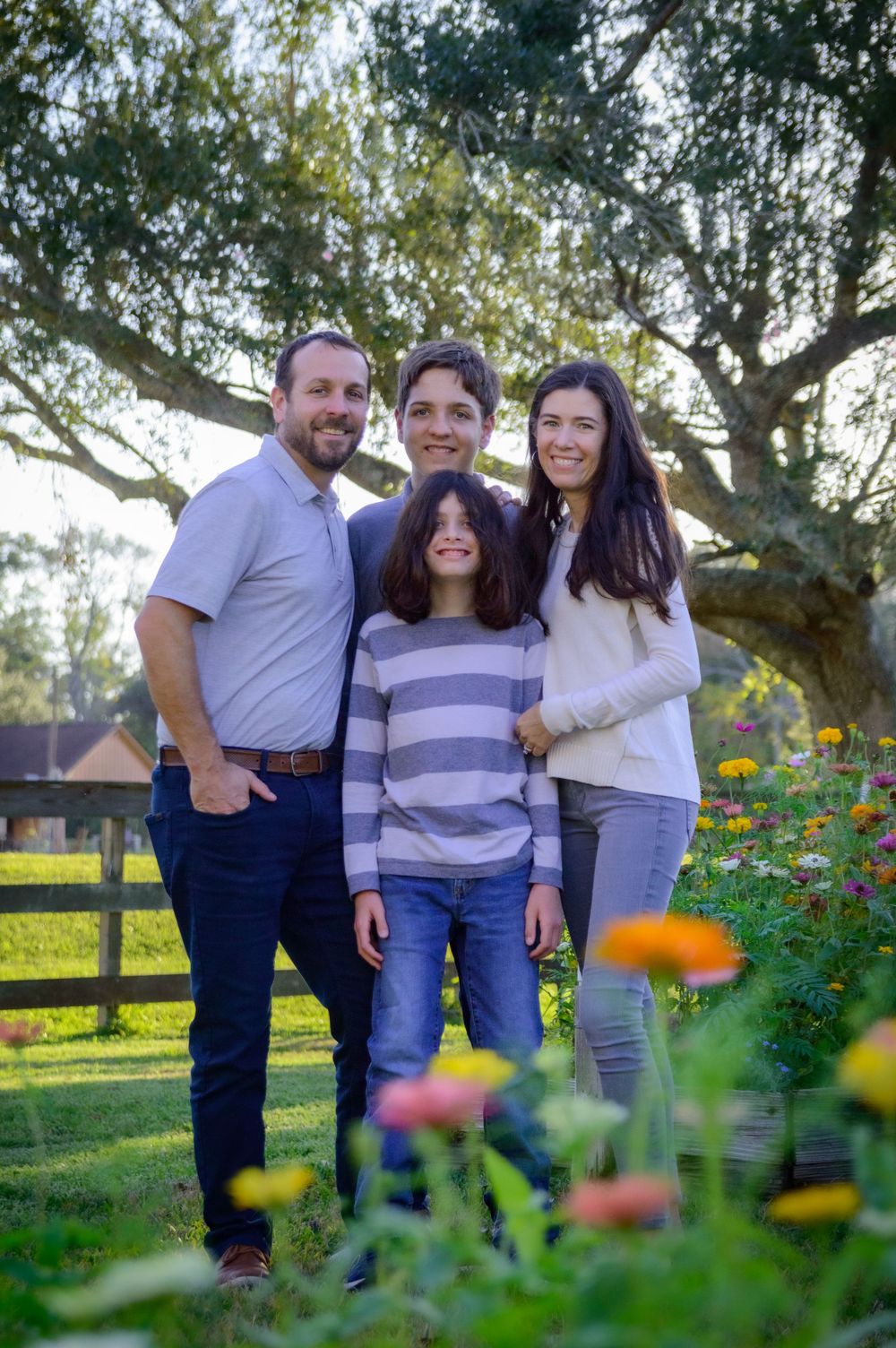 A family of four poses together in front of blooming wildflowers and a wooden fence.