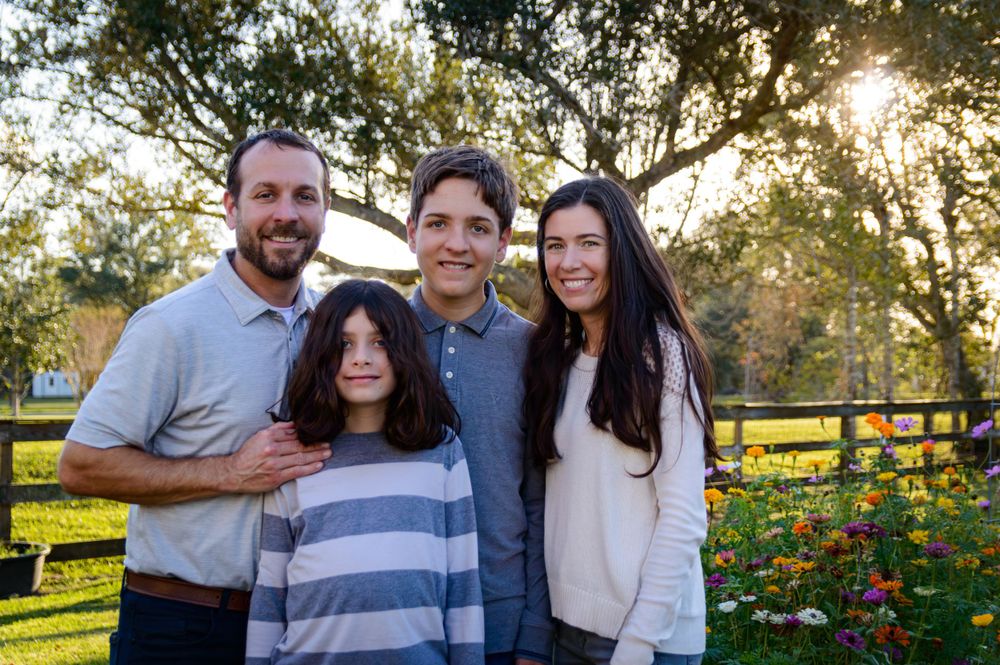 A family of four poses together in front of a sunset-lit garden with blooming flowers.