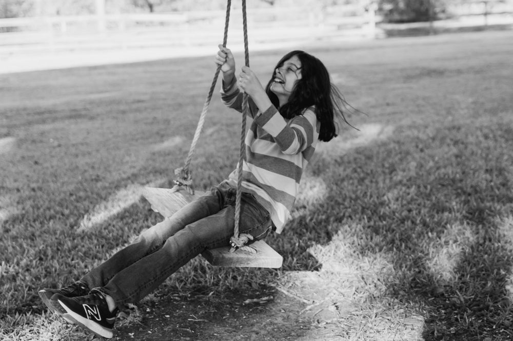 Child enjoying a swing outdoors in black and white photography.