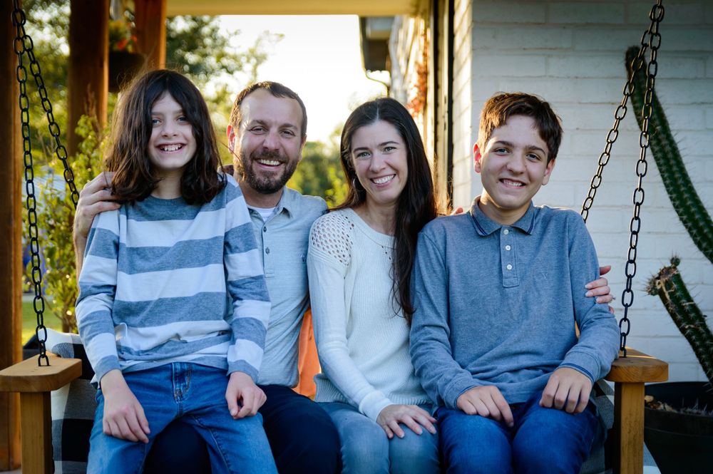 Family of four sitting together on a porch swing during an outdoor photo session.