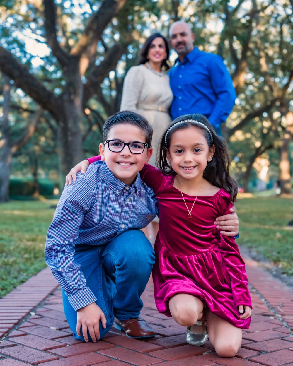 Two children in casual attire pose playfully on a brick path surrounded by autumn trees in a park setting.