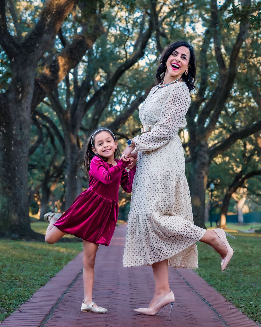 A playful moment captured on a brick pathway with two people in burgundy and polka dot dresses dancing together.