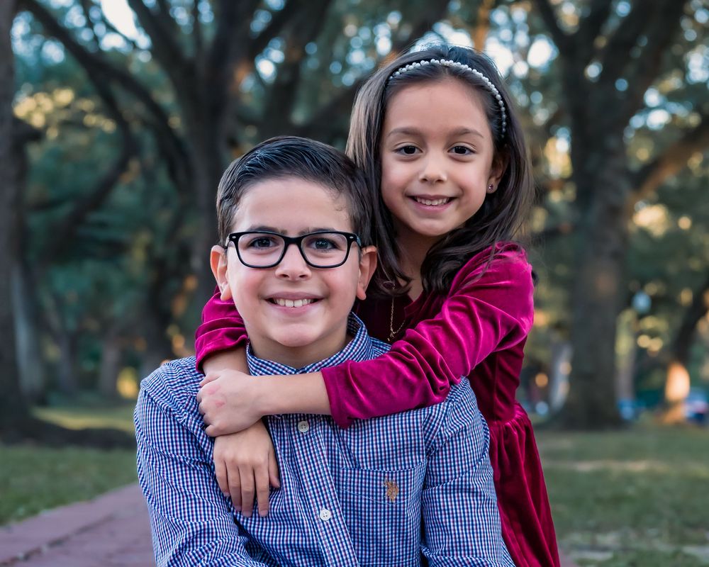 Two siblings share a joyful hug while posing outdoors in coordinated outfits.