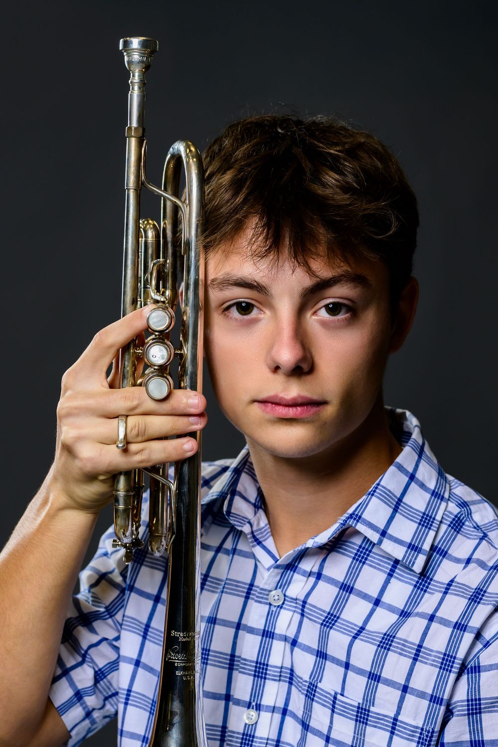 Four sequential photos show someone in a blue checkered shirt posing with a trumpet against a dark background.