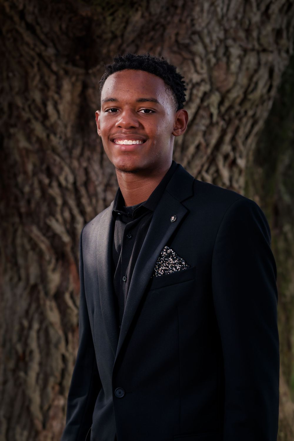 A portrait session in formal black attire against a textured tree bark background.