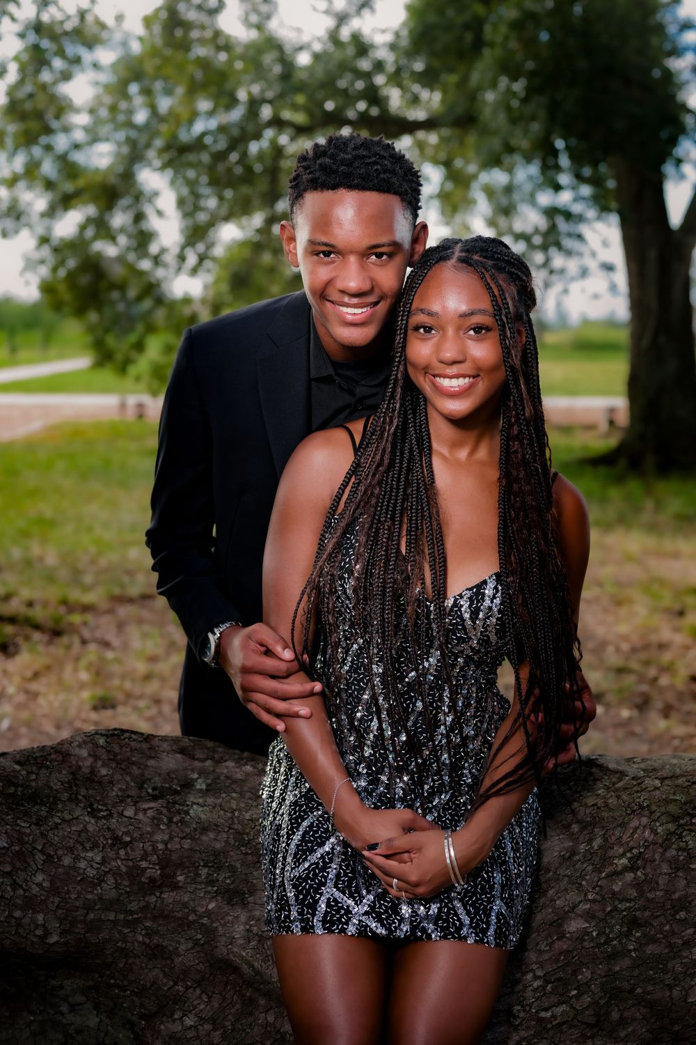 A couple poses together outdoors in a natural setting with trees in the background.
