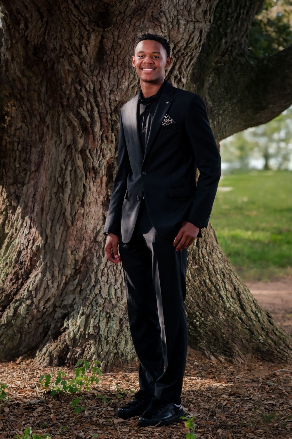 A series of outdoor portrait photos showing someone in a dark suit posing next to a large tree trunk.