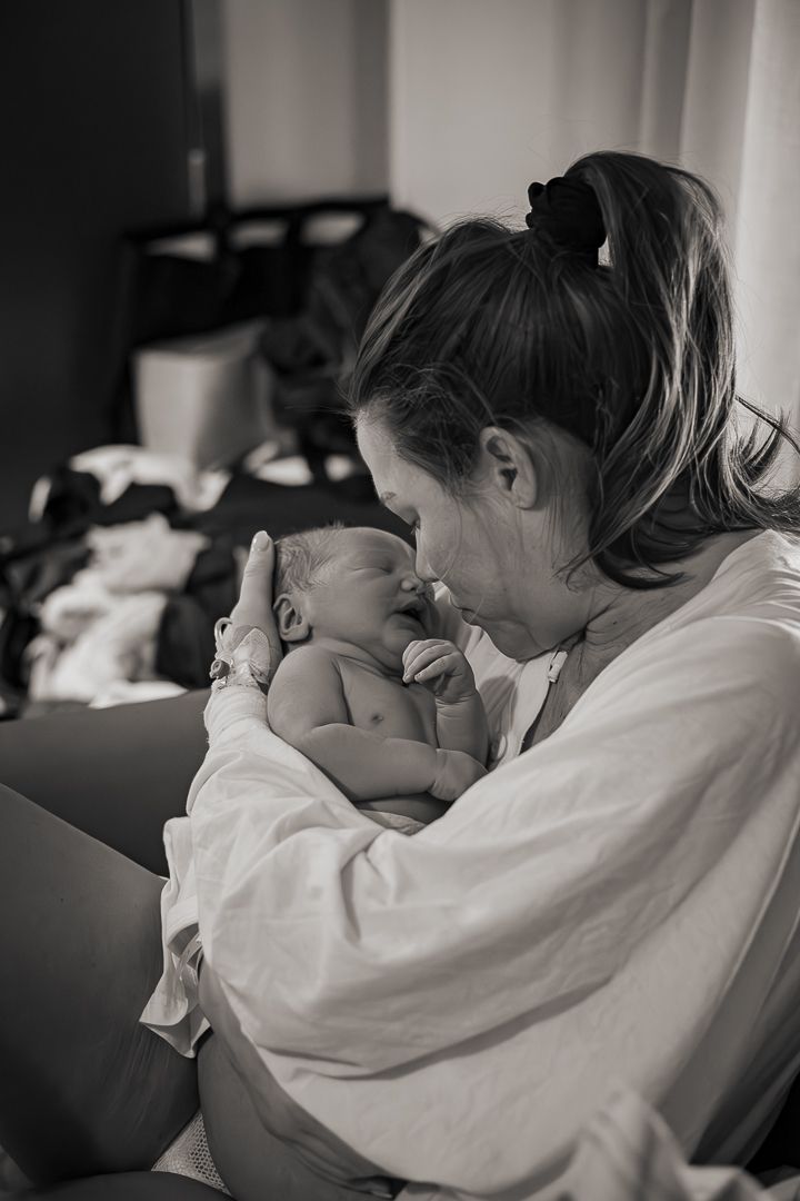 A tender black and white photograph shows a parent cradling and looking lovingly at their sleeping newborn baby.