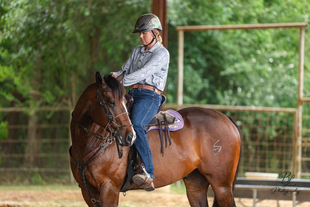 Young rider in helmet sits atop a bay horse in an outdoor arena during an equestrian training session.