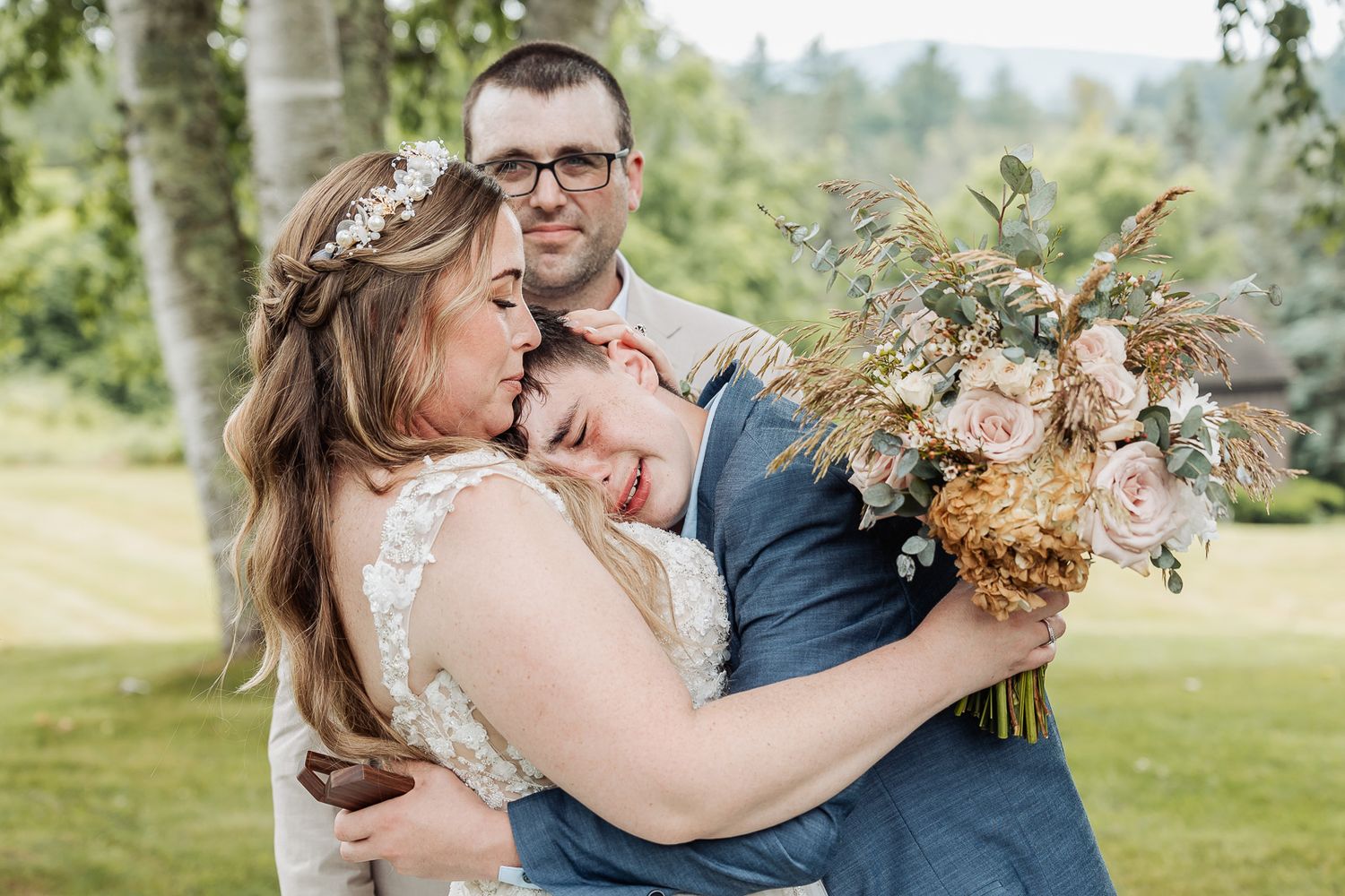 Romantic outdoor wedding photo with couple embracing while holding floral bouquet.
