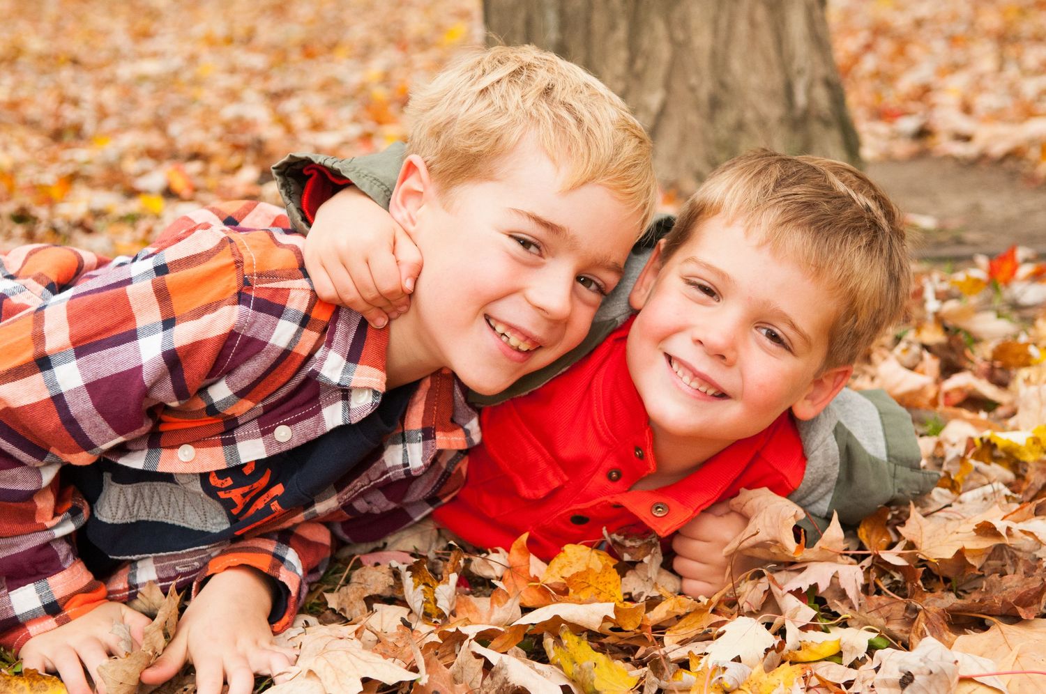 Two children laying in autumn leaves smile at the camera during a fall photoshoot.
