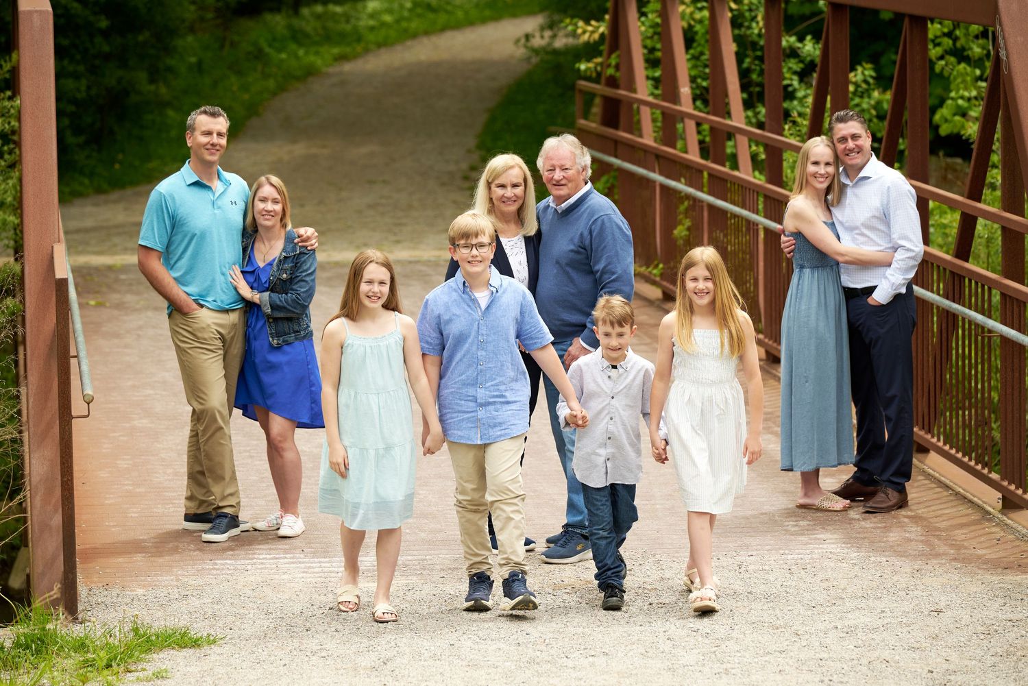 A group of people stand together on a wooden bridge surrounded by greenery in casual summer attire.