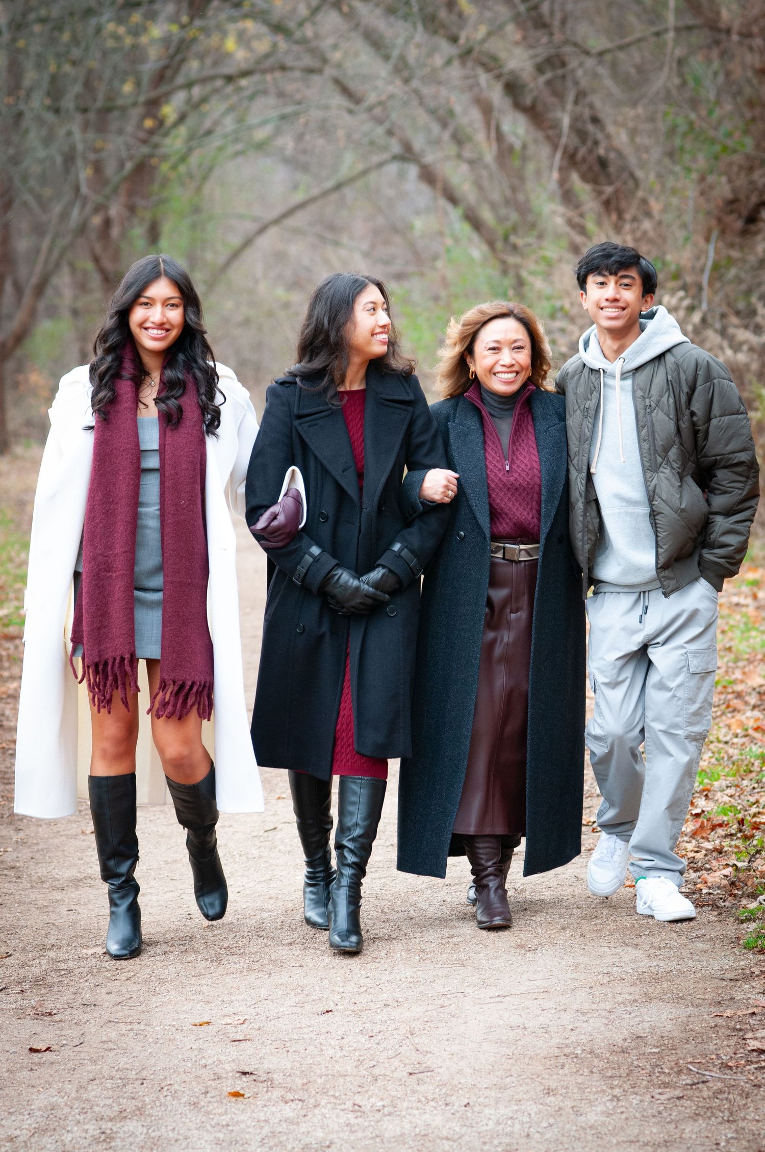 Group of friends walking together on a tree-lined autumn path wearing stylish winter coats in burgundy and black.