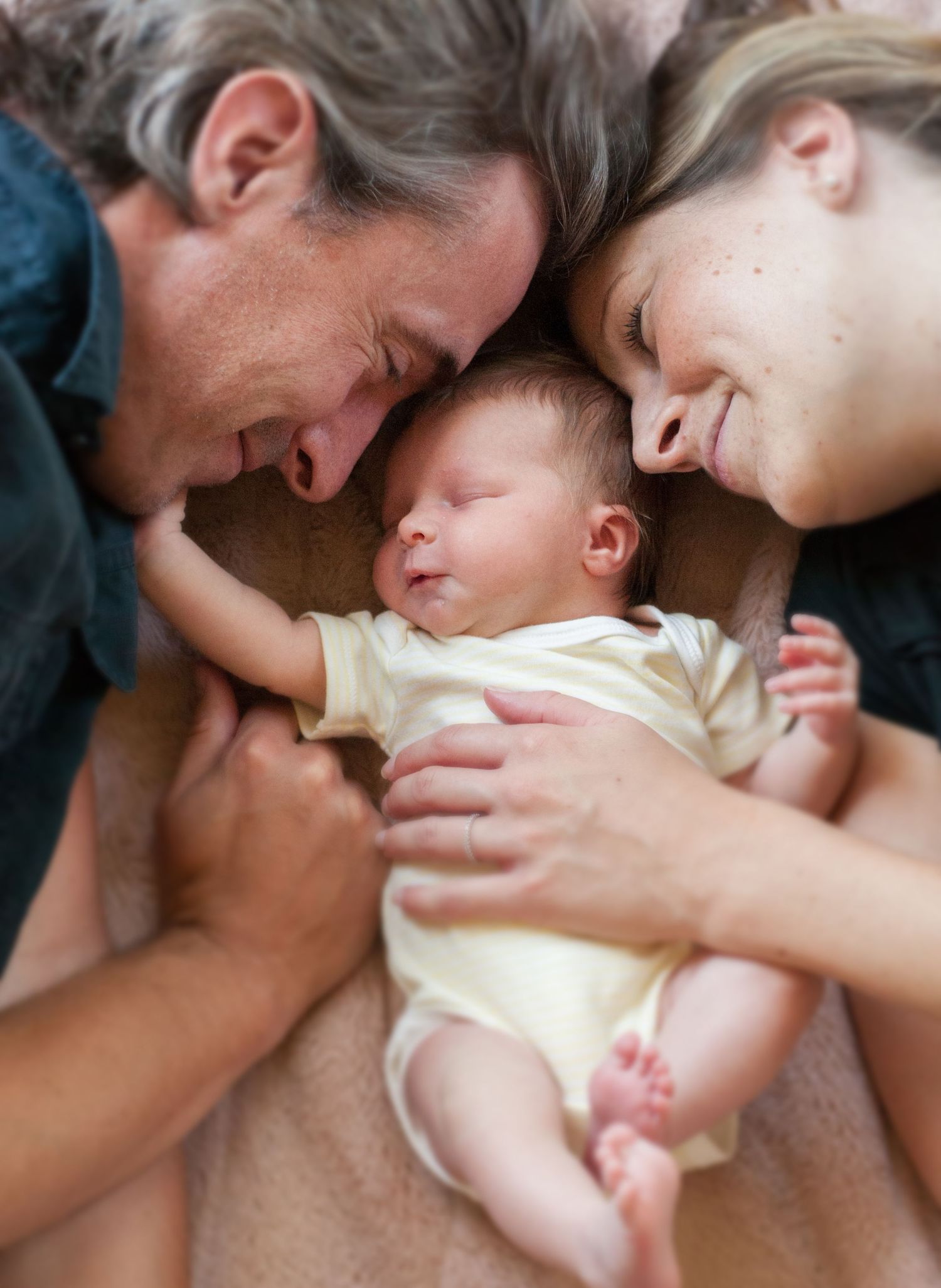 A tender moment with a sleeping newborn baby wearing a yellow onesie.