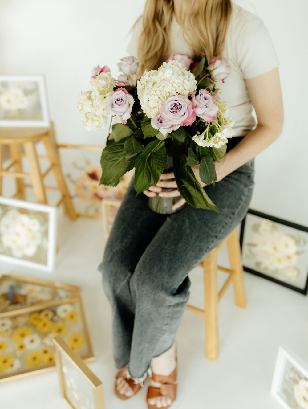 Woman sitting on a stool holding a bouquet of white hydrangeas and pink roses in a floral studio.