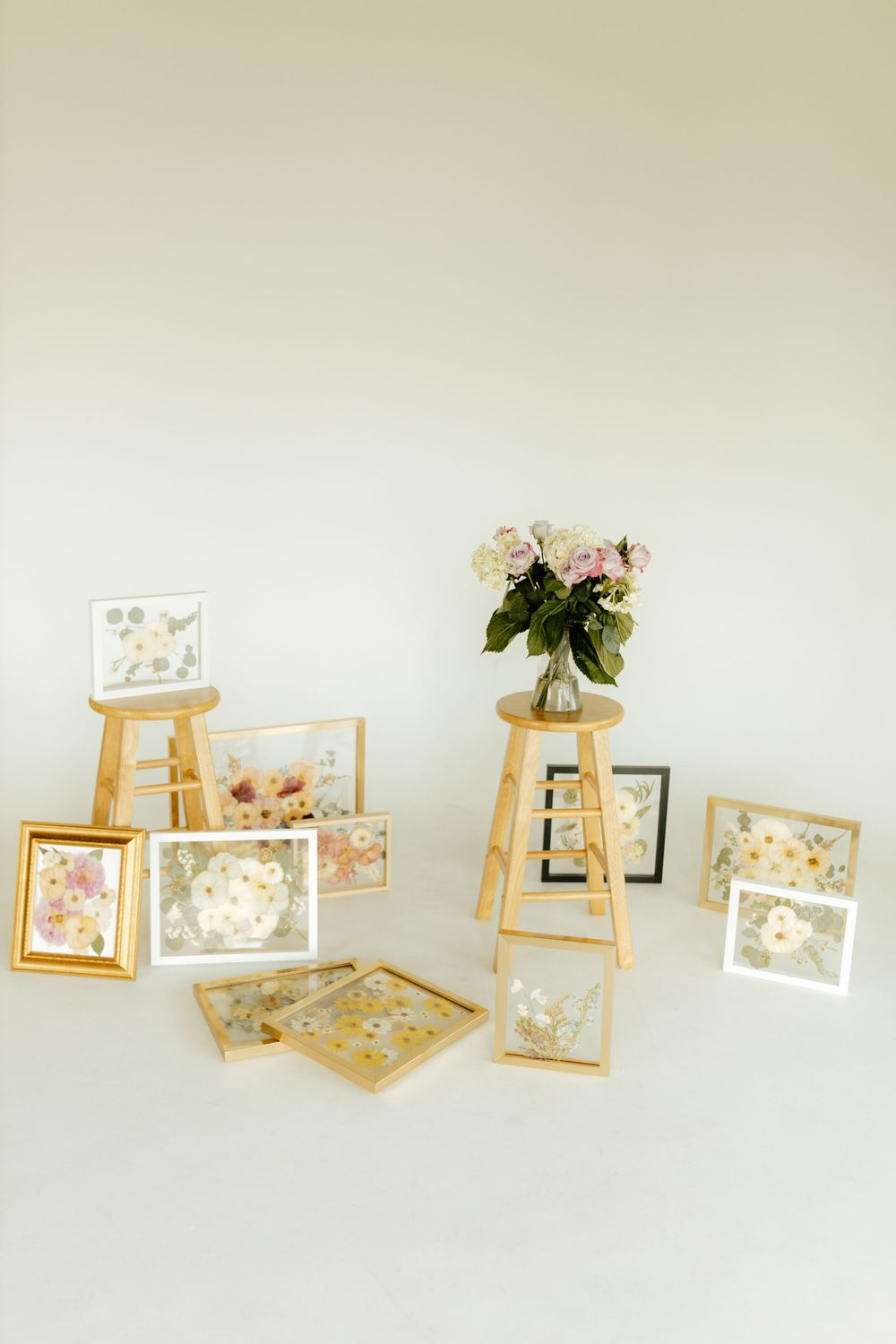 Collection of framed pressed flower artworks displayed on wooden stools with fresh roses.