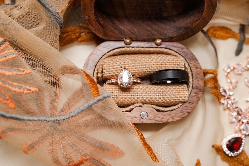 Wedding rings displayed in rustic wooden box with burlap lining and decorative details.