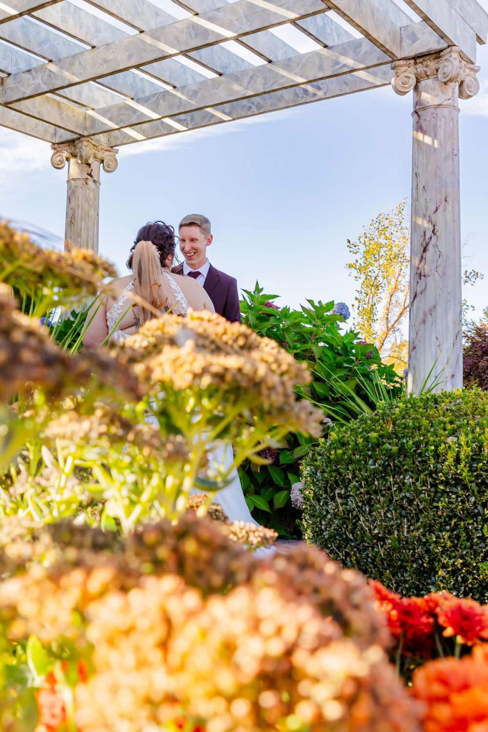 A couple shares an intimate moment under a white pergola surrounded by autumn flowers.