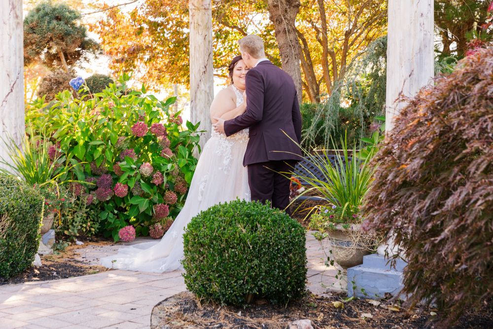 A couple shares a moment under white pillars surrounded by landscaped gardens.