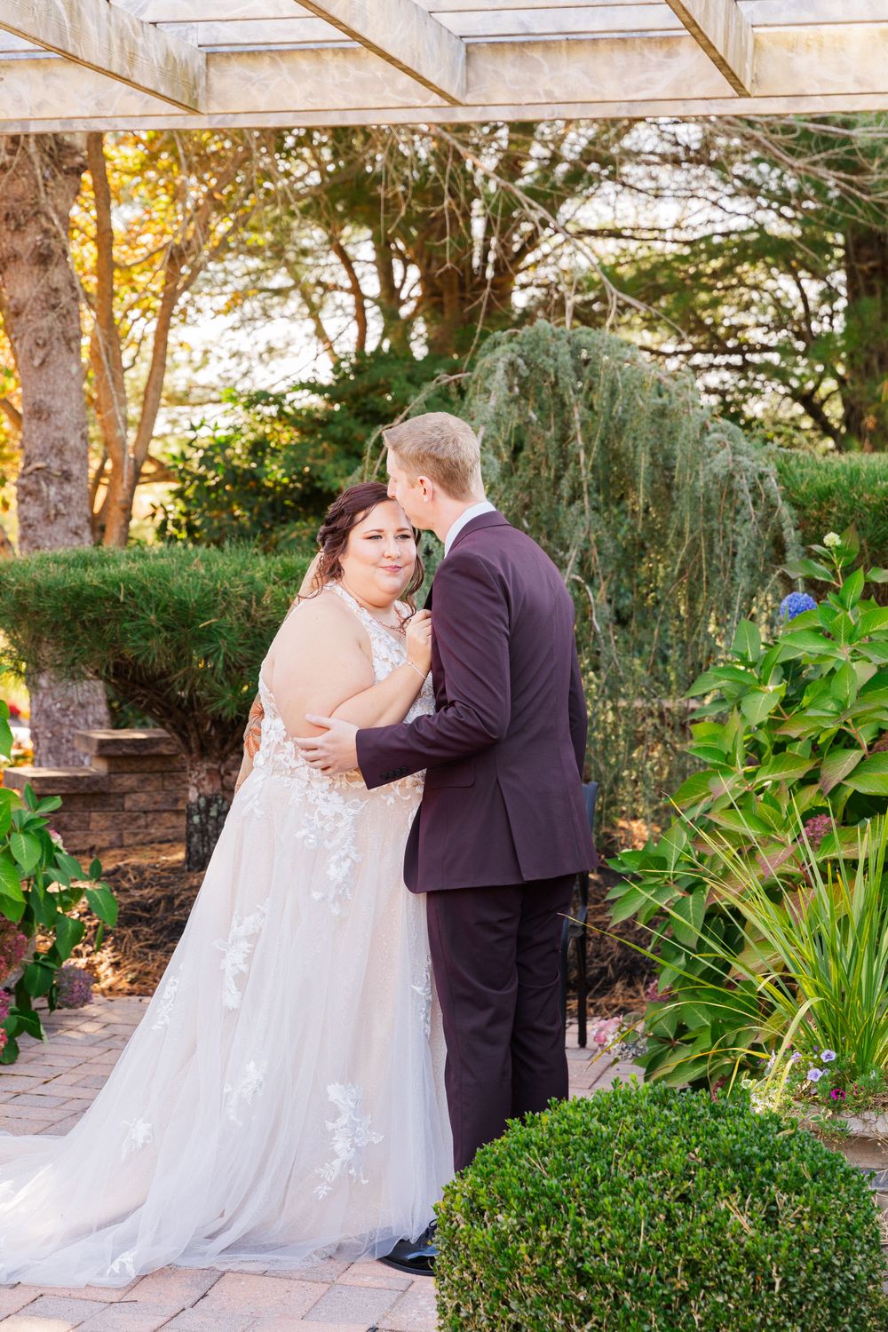 A romantic wedding moment captured in a garden setting with lush greenery and sunlight filtering through the trees.