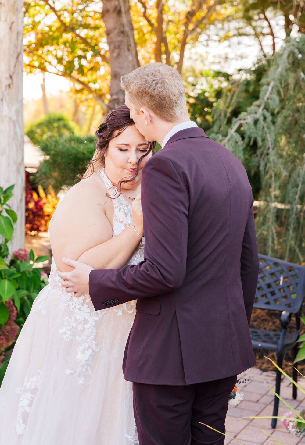Romantic wedding moment in a garden with burgundy suit and white dress.