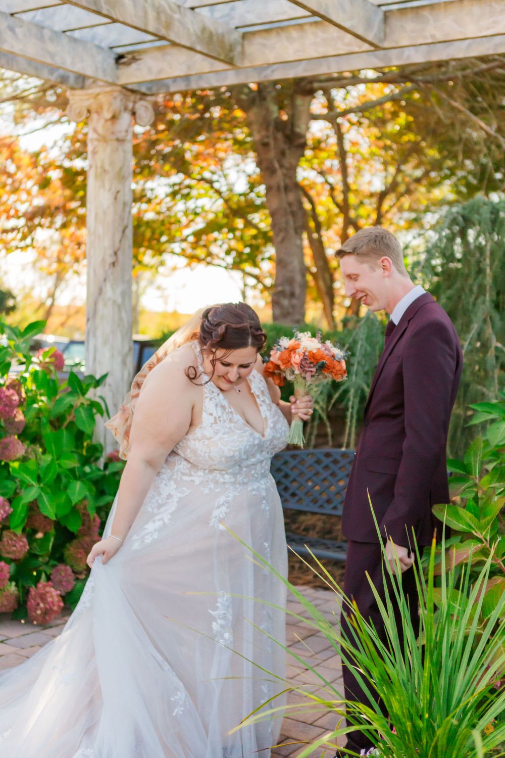 Couple shares intimate moment under garden pergola surrounded by lush greenery and fall foliage.