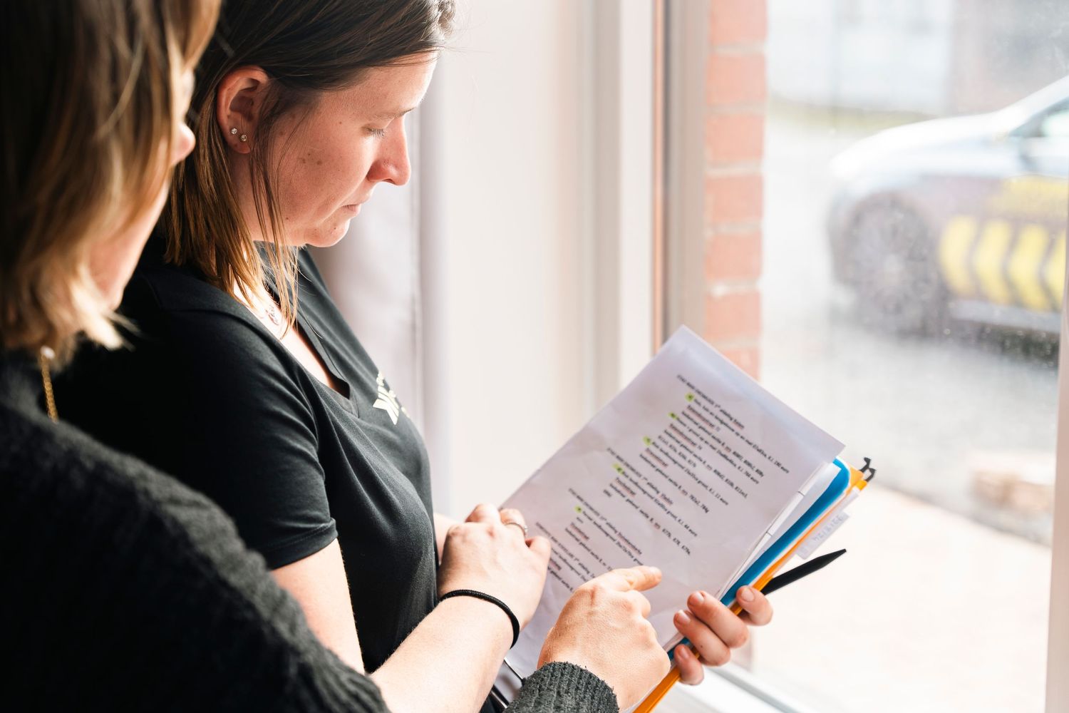 Professional reviewing paperwork while standing near window.