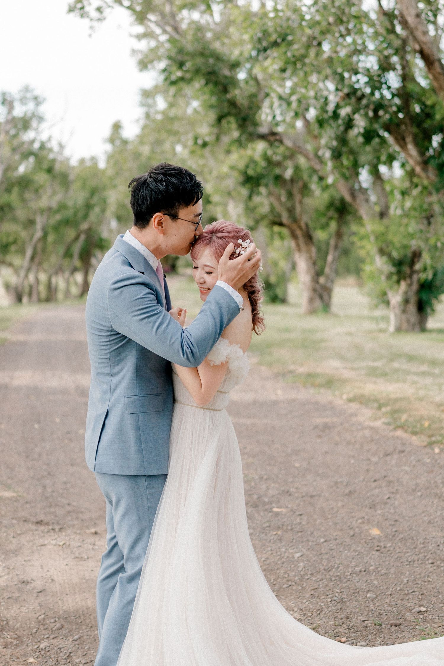 A tender moment between newlyweds on a tree-lined path during their wedding day.