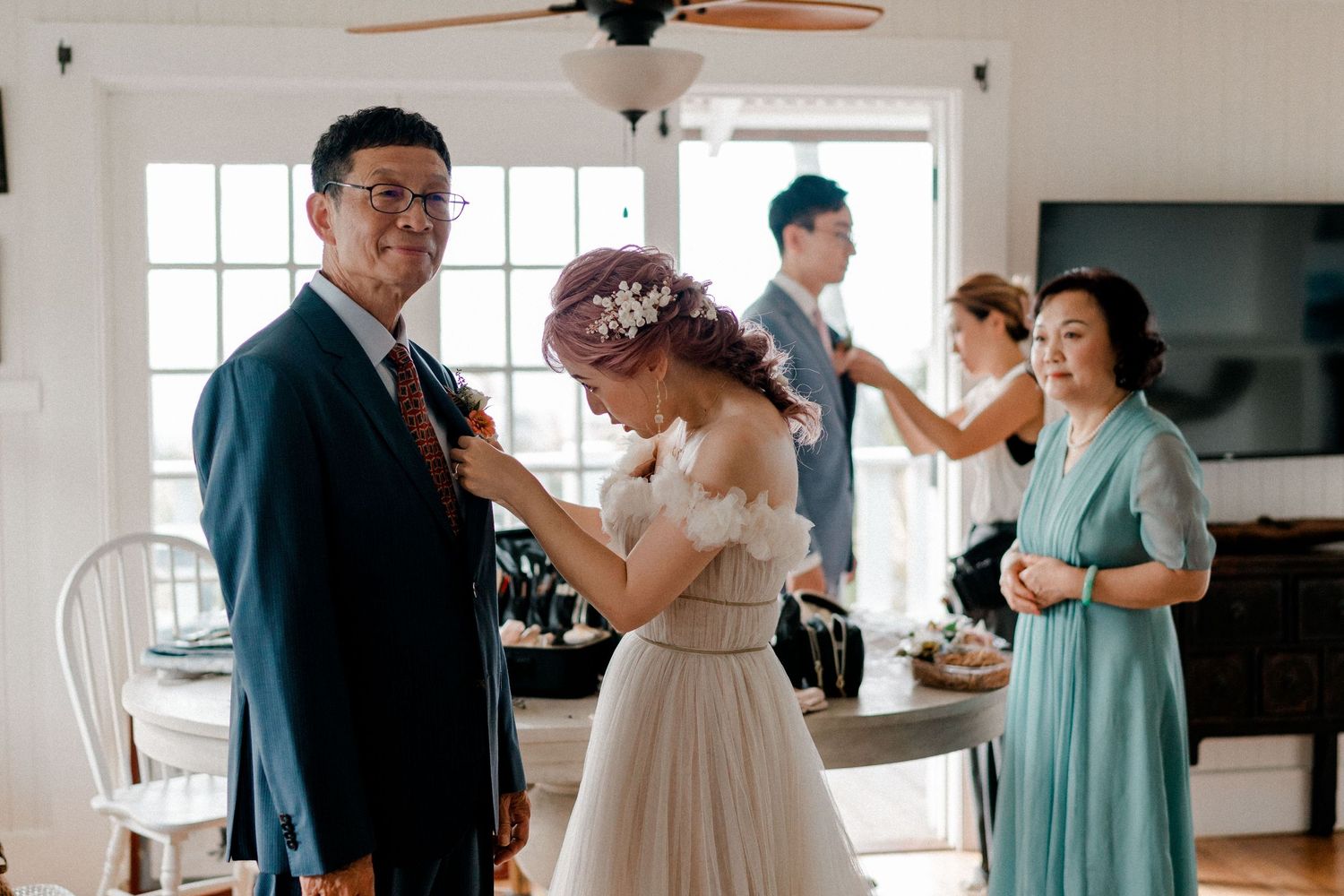 Wedding preparations in a bright indoor setting with guests in formal attire.