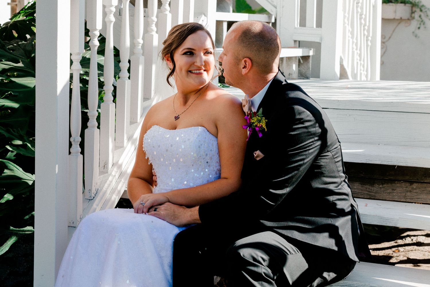 A couple shares an intimate moment on white porch steps during their wedding day.