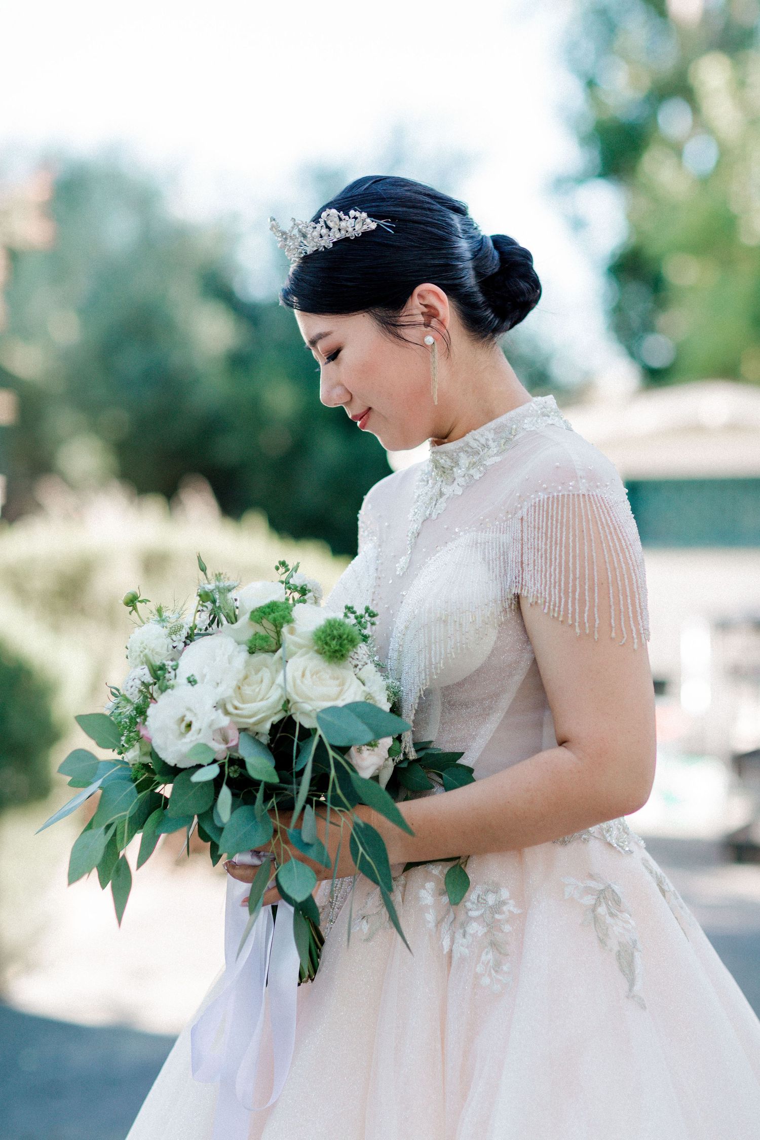 A bride in vintage-inspired dress holds a bouquet of white flowers and eucalyptus leaves.
