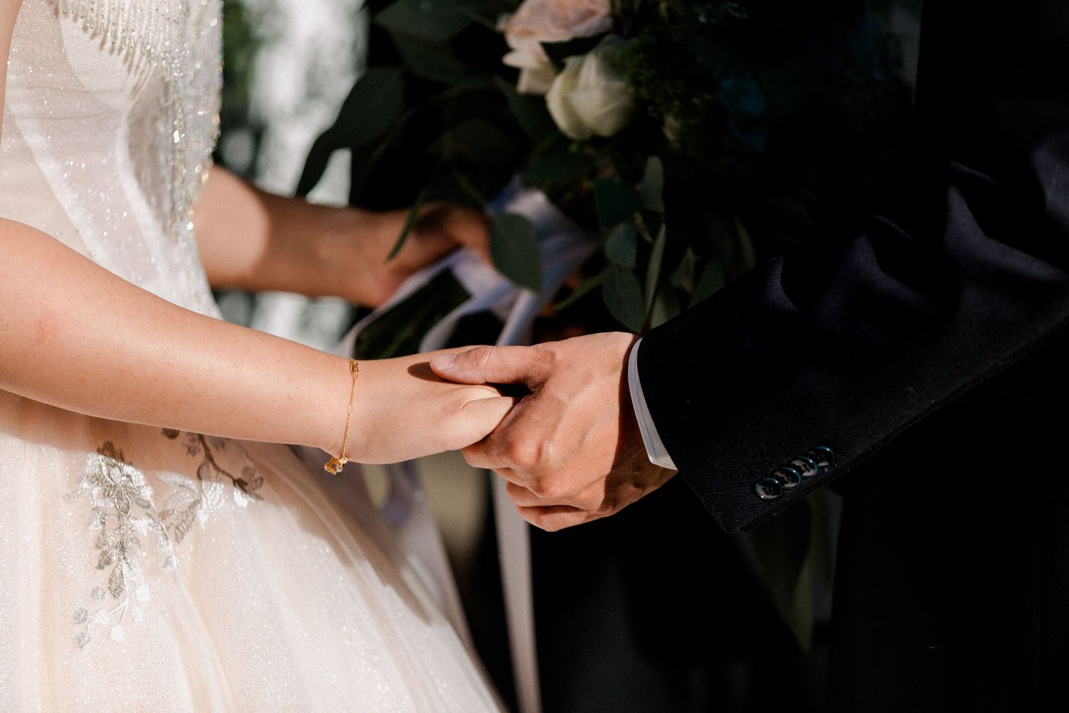 Close-up of hands joined together during a wedding ceremony with lace dress details visible.