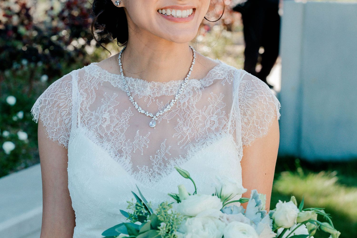 Bride's bouquet of white roses and green eucalyptus against a delicate lace wedding dress.