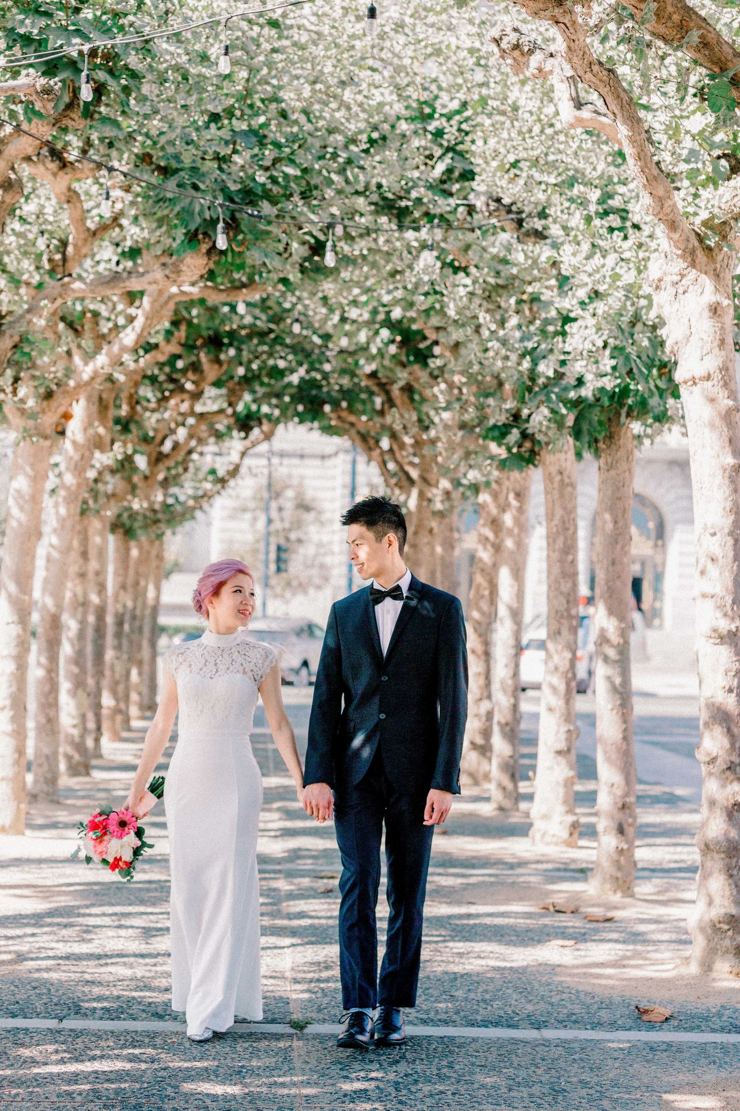 A romantic wedding photo taken under a canopy of blossoming trees with pink florals.