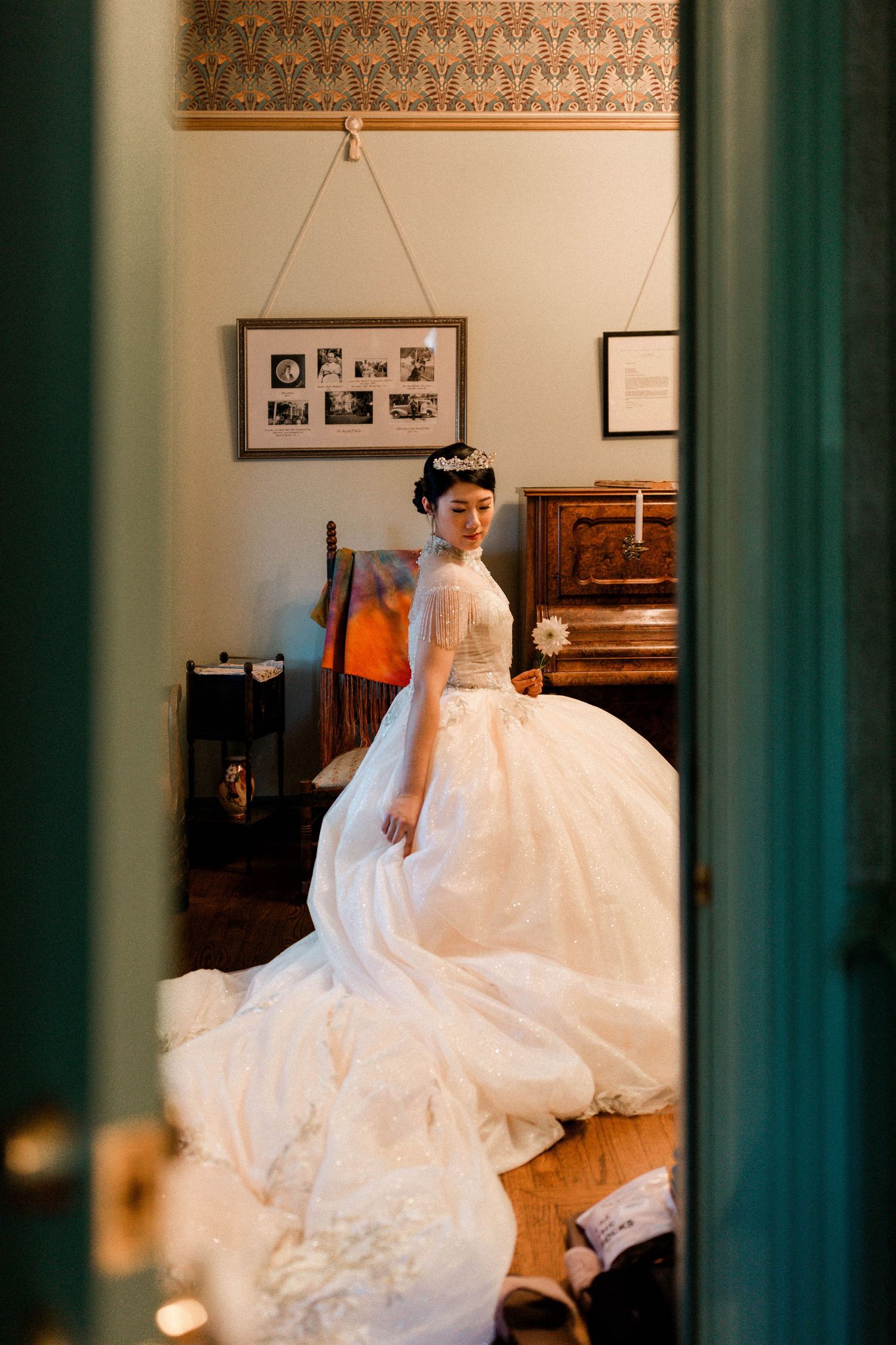 A stunning white wedding gown with a long train is displayed in a room with vintage decor and a piano.