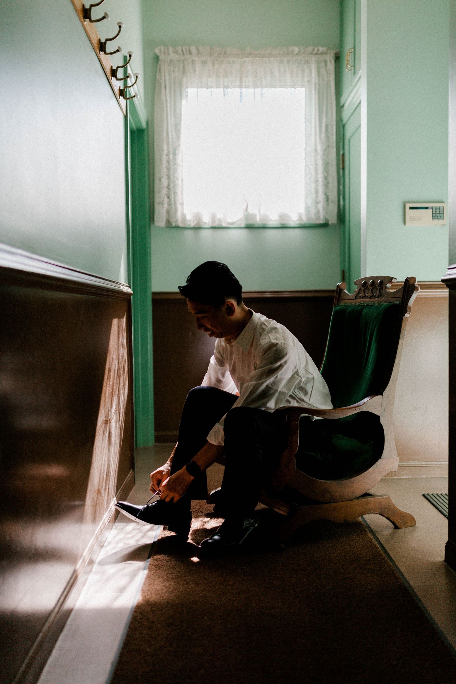 A quiet moment captured as someone ties their shoes in a mint green room with lace curtains.