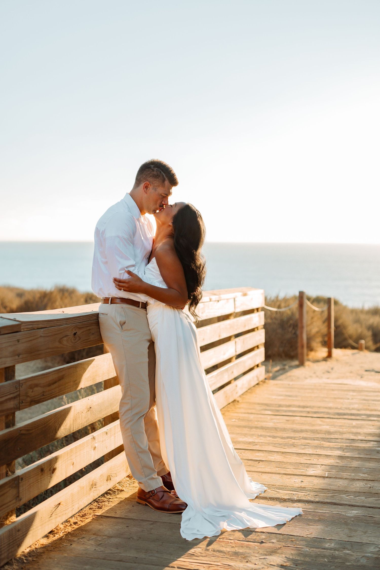 A couple sharing an intimate moment on a wooden boardwalk by the ocean.