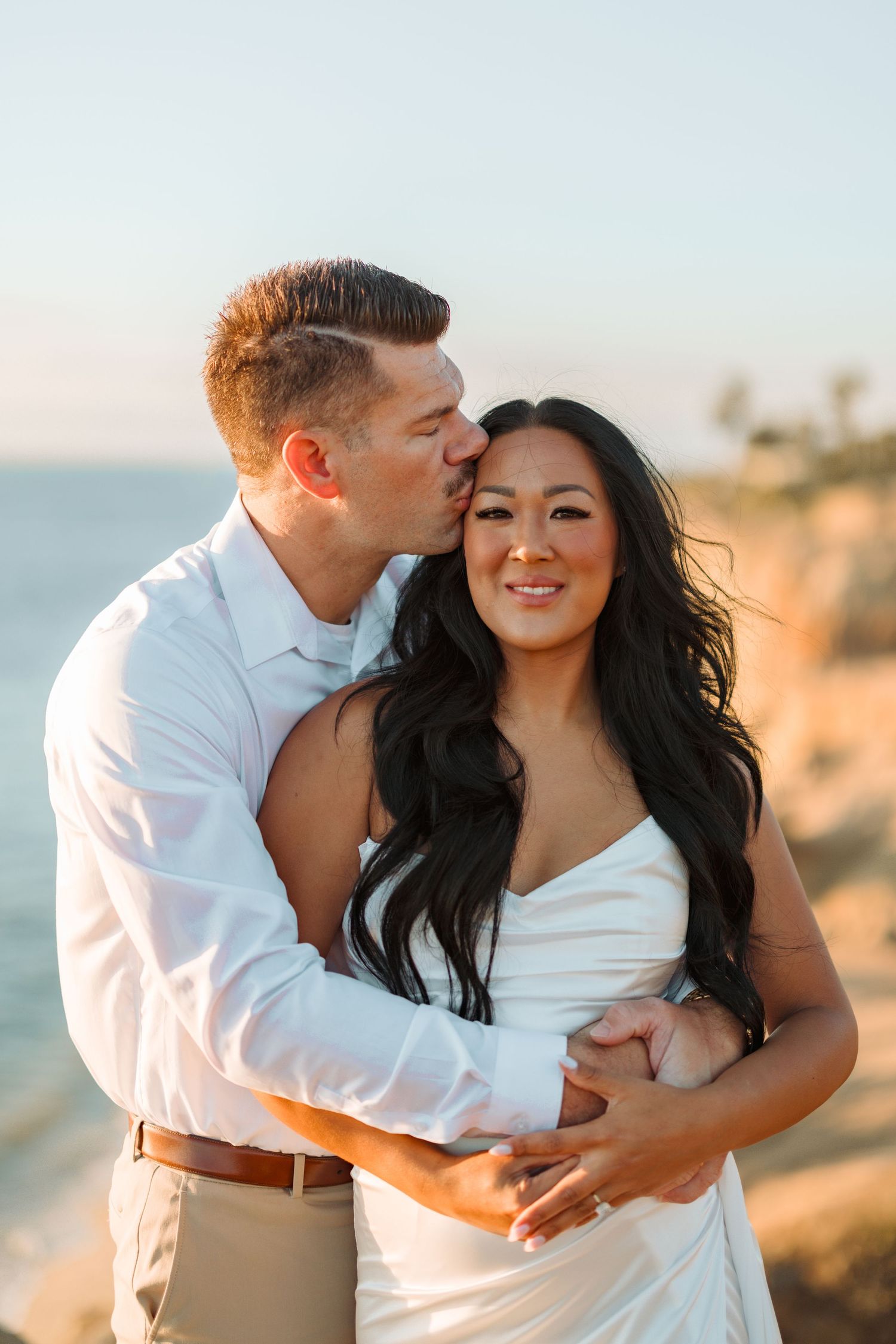 A romantic sunset engagement photo on a coastal cliff.