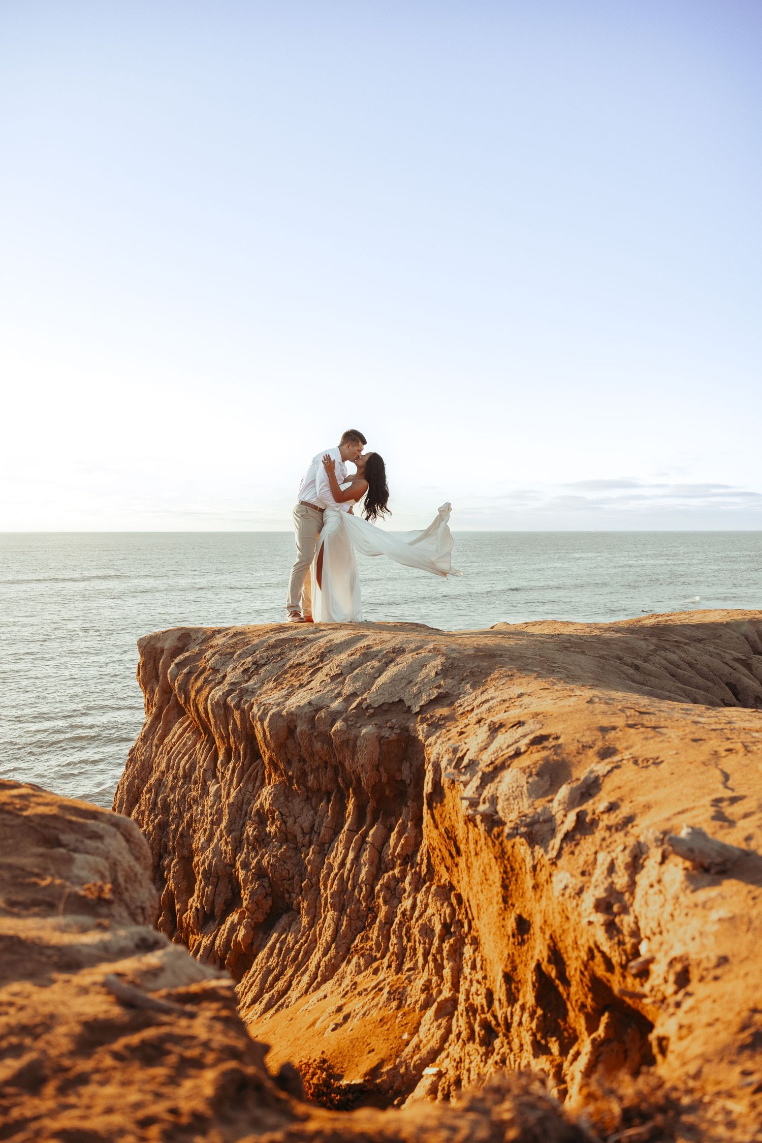 A romantic silhouette of a couple on a dramatic oceanside cliff at sunset.
