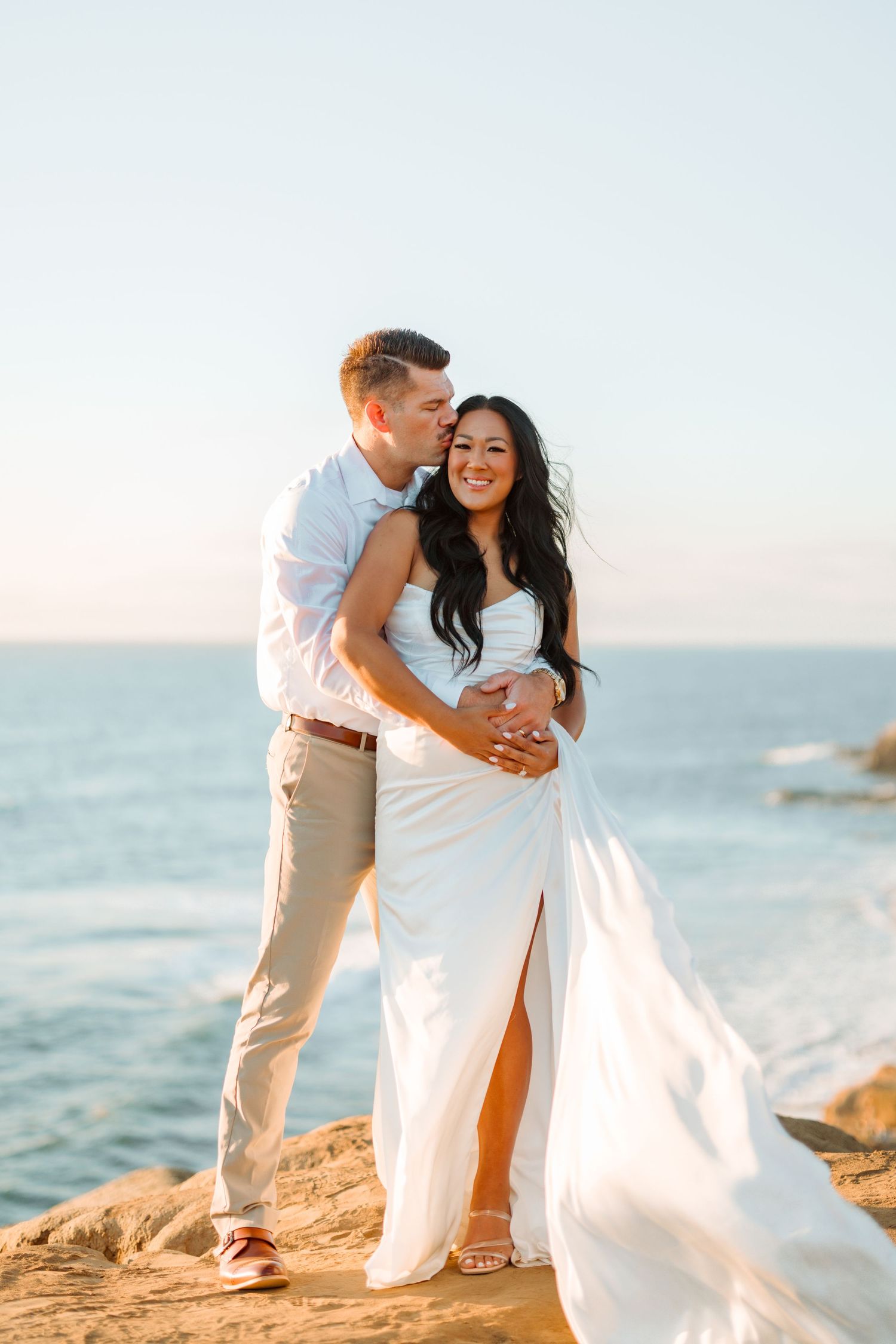 A candid moment between a couple laughing on coastal rocks at sunset.