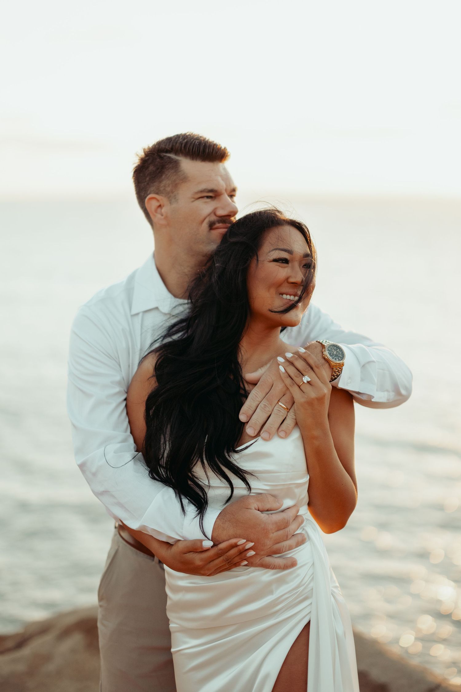 Intimate embrace on beach rocks during golden hour photoshoot.