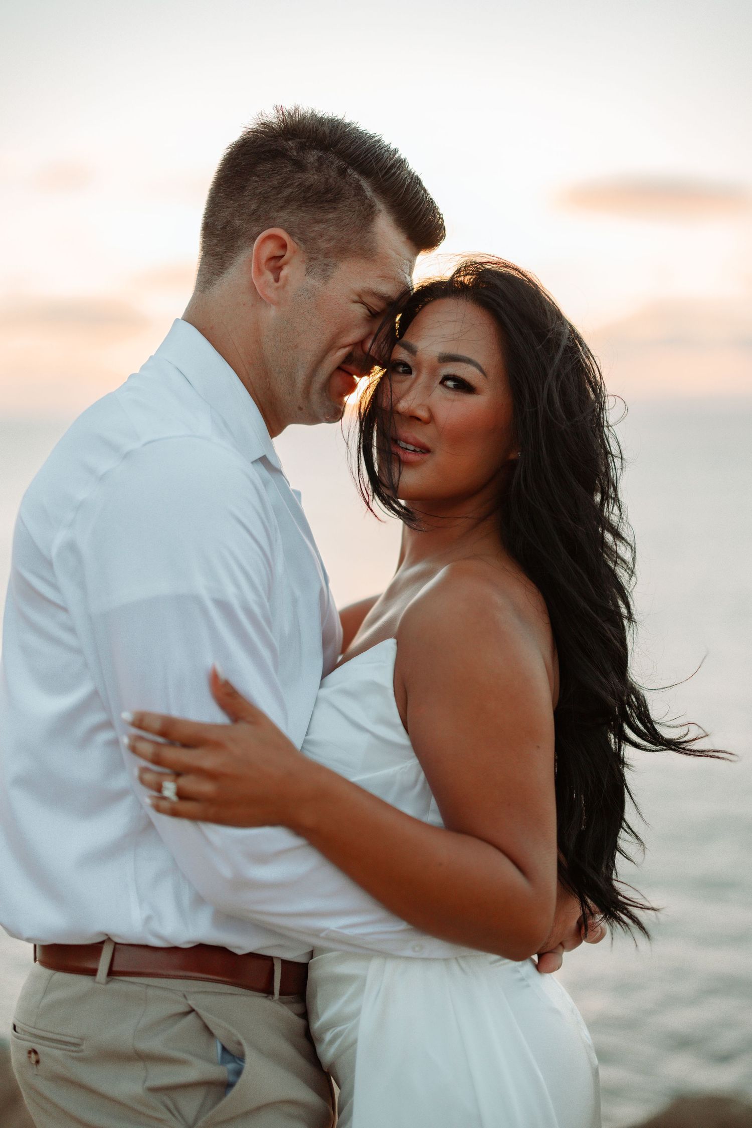 Intimate couple's portrait against ocean backdrop at sunset.