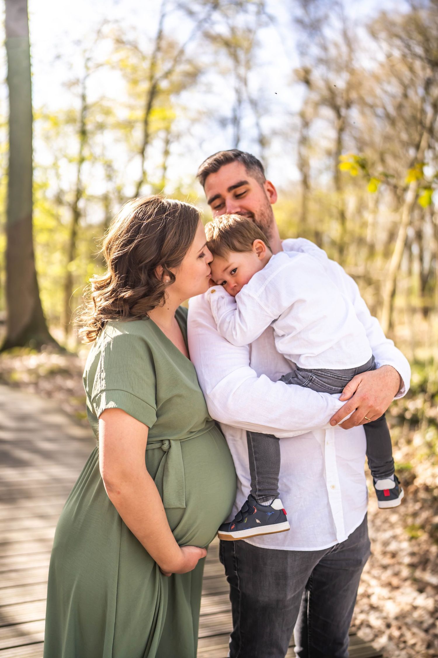 A tender family moment captured in sunlit woods with wooden walkway.