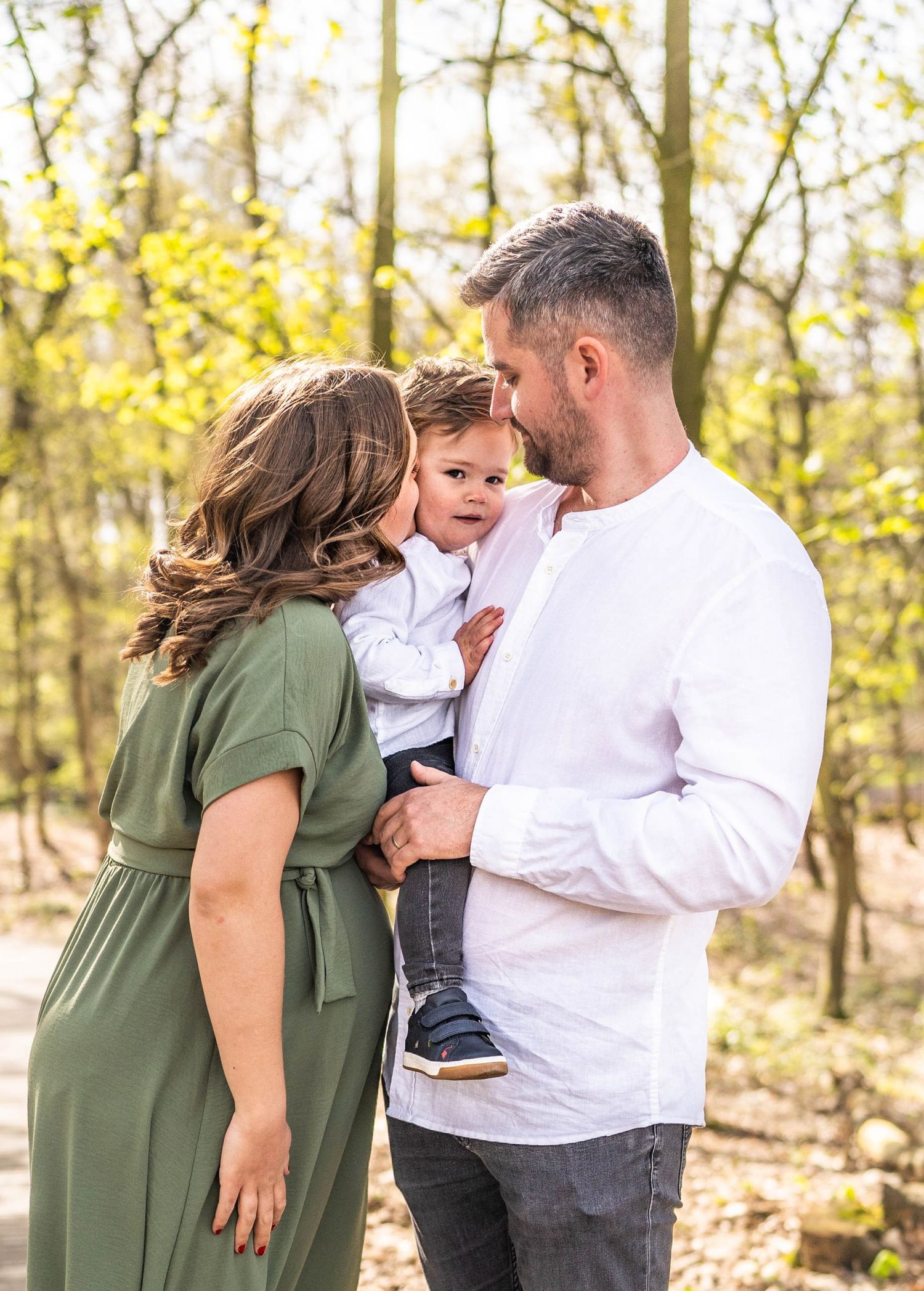A family shares a loving moment together in a sun-dappled forest setting.