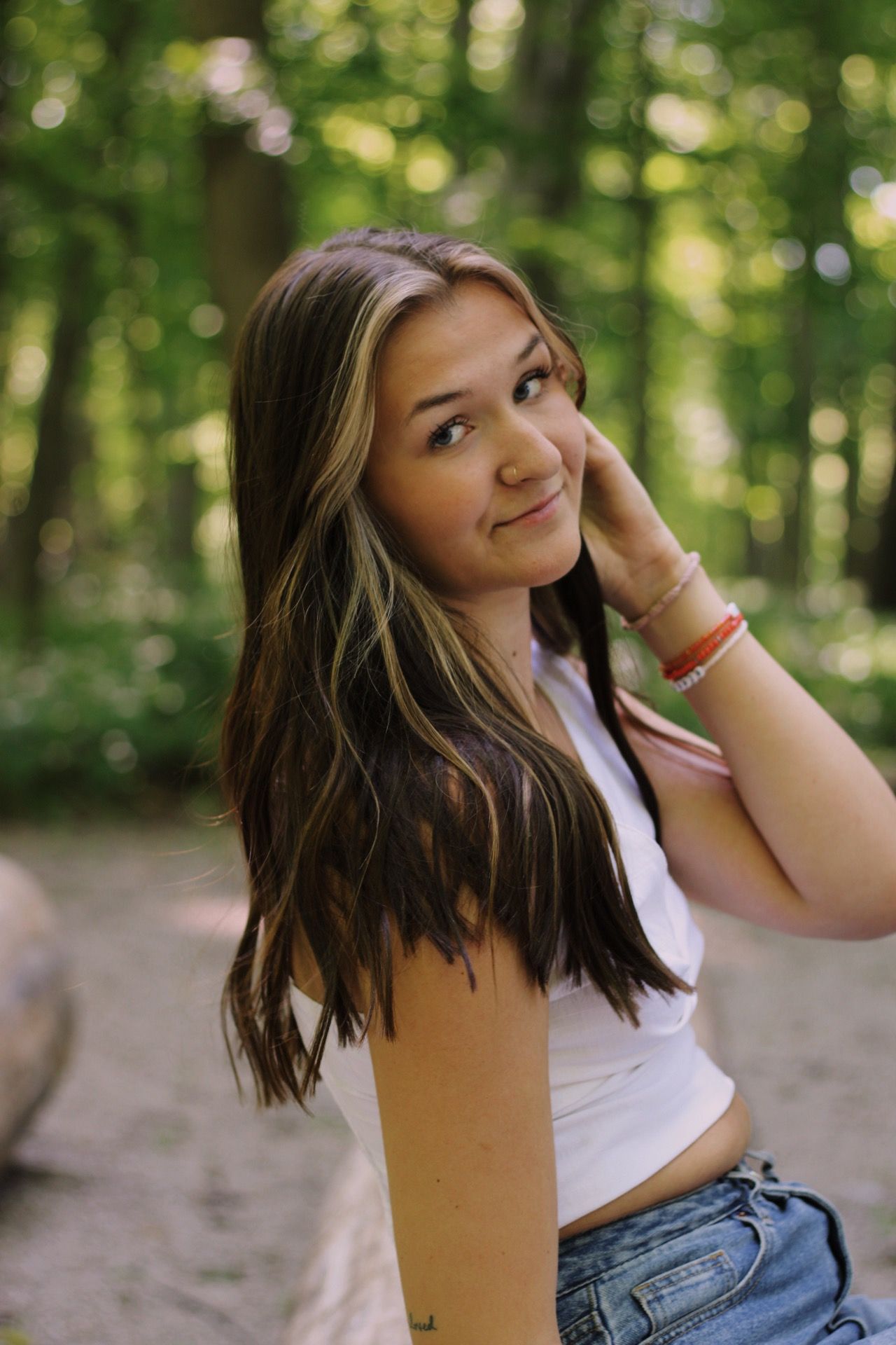 A young woman in a portrait photo smiling softly with a trees in the background