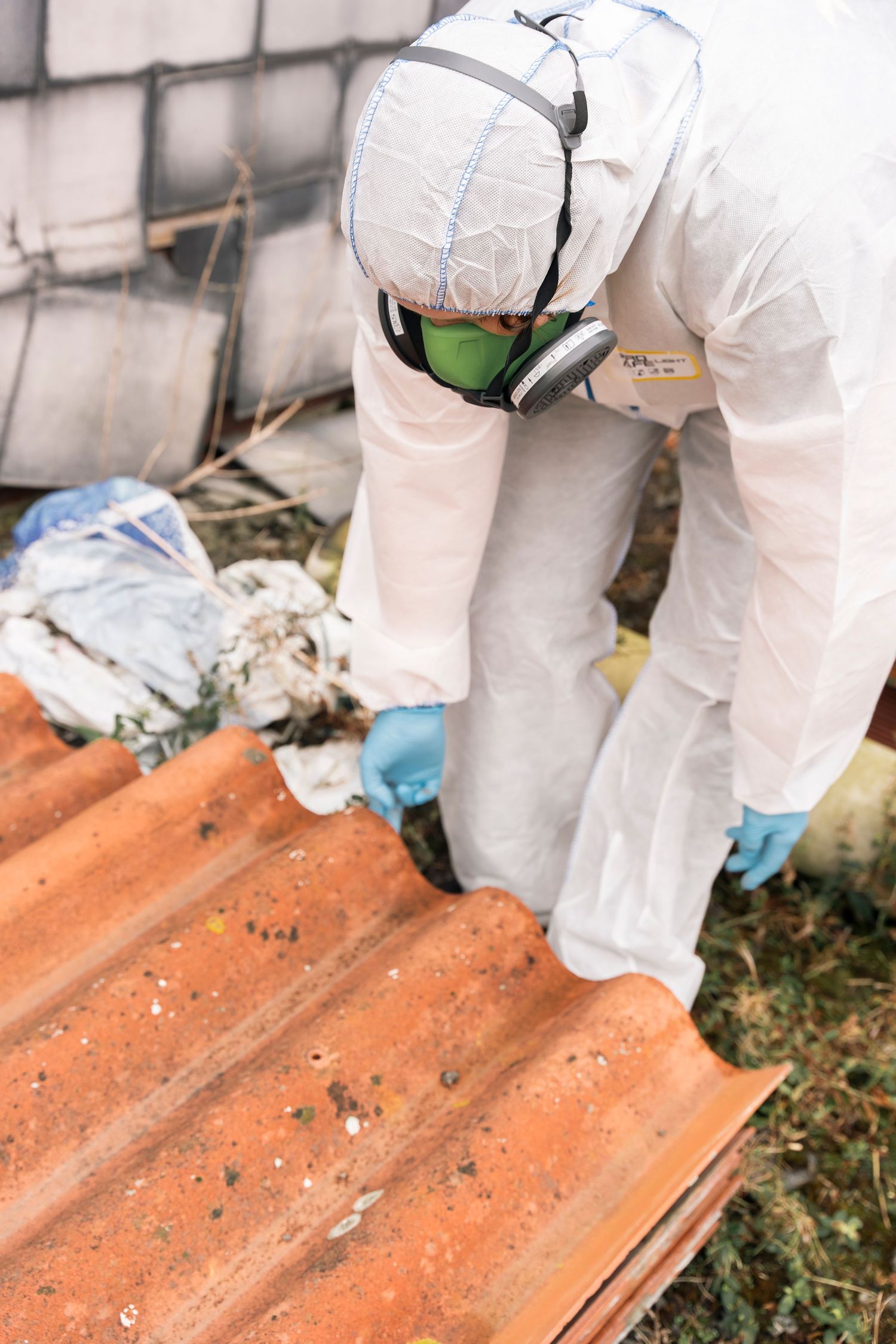 Worker in protective hazmat suit and mask inspecting corrugated metal surfaces.