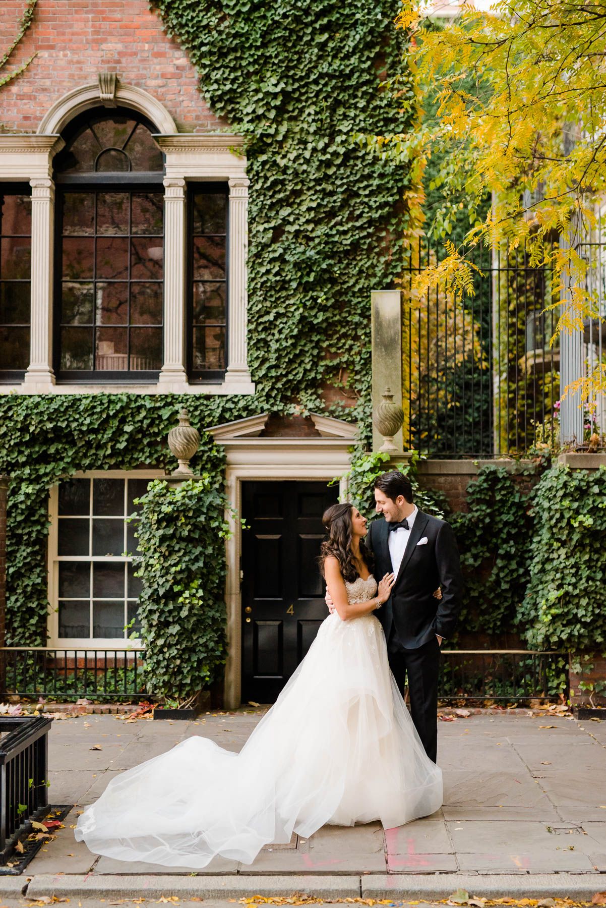 Elegant bride and groom embrace in front of ivy-covered brick building with classical architecture.